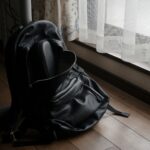 a black backpack sitting on the floor in front of a window
