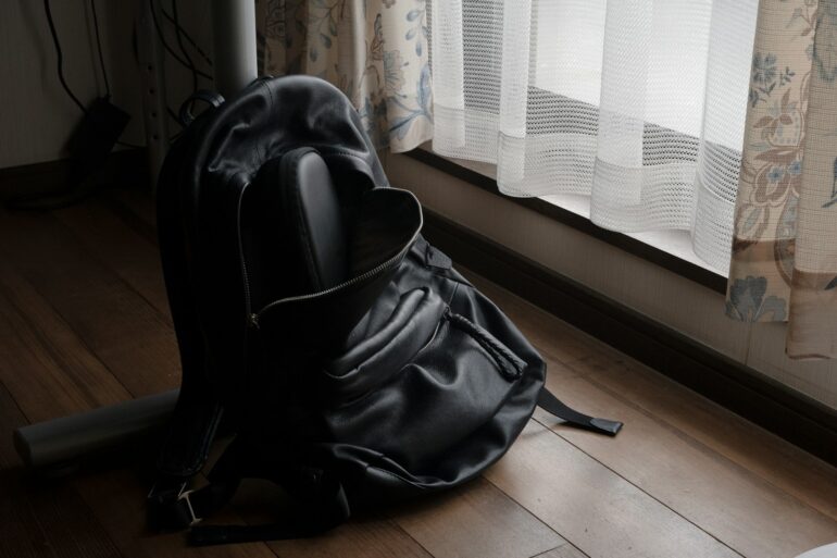 a black backpack sitting on the floor in front of a window