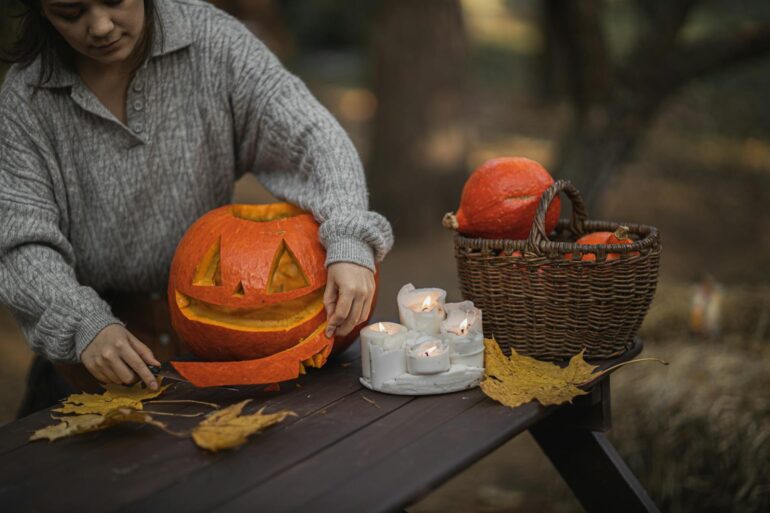 Halloween, Deko, Woman carving a pumpkin outdoors with candles and autumn leaves. Perfect for Halloween or Thanksgiving.