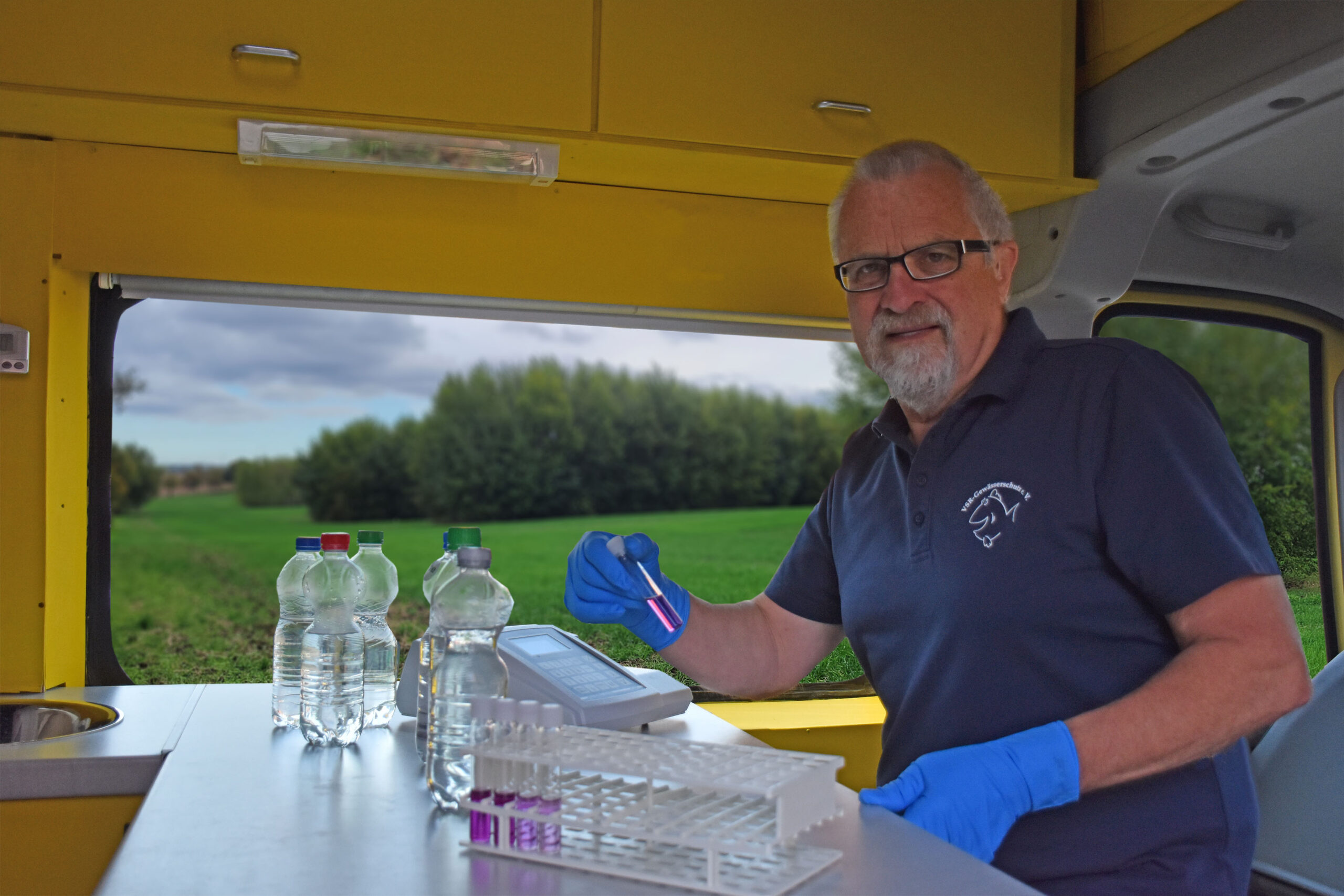 Harald Gülzow analysiert eine Wasserprobe, Hintergrund Agroforst. Foto: Ruben Wiltsch