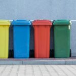 four assorted-color trash bins beside gray wall